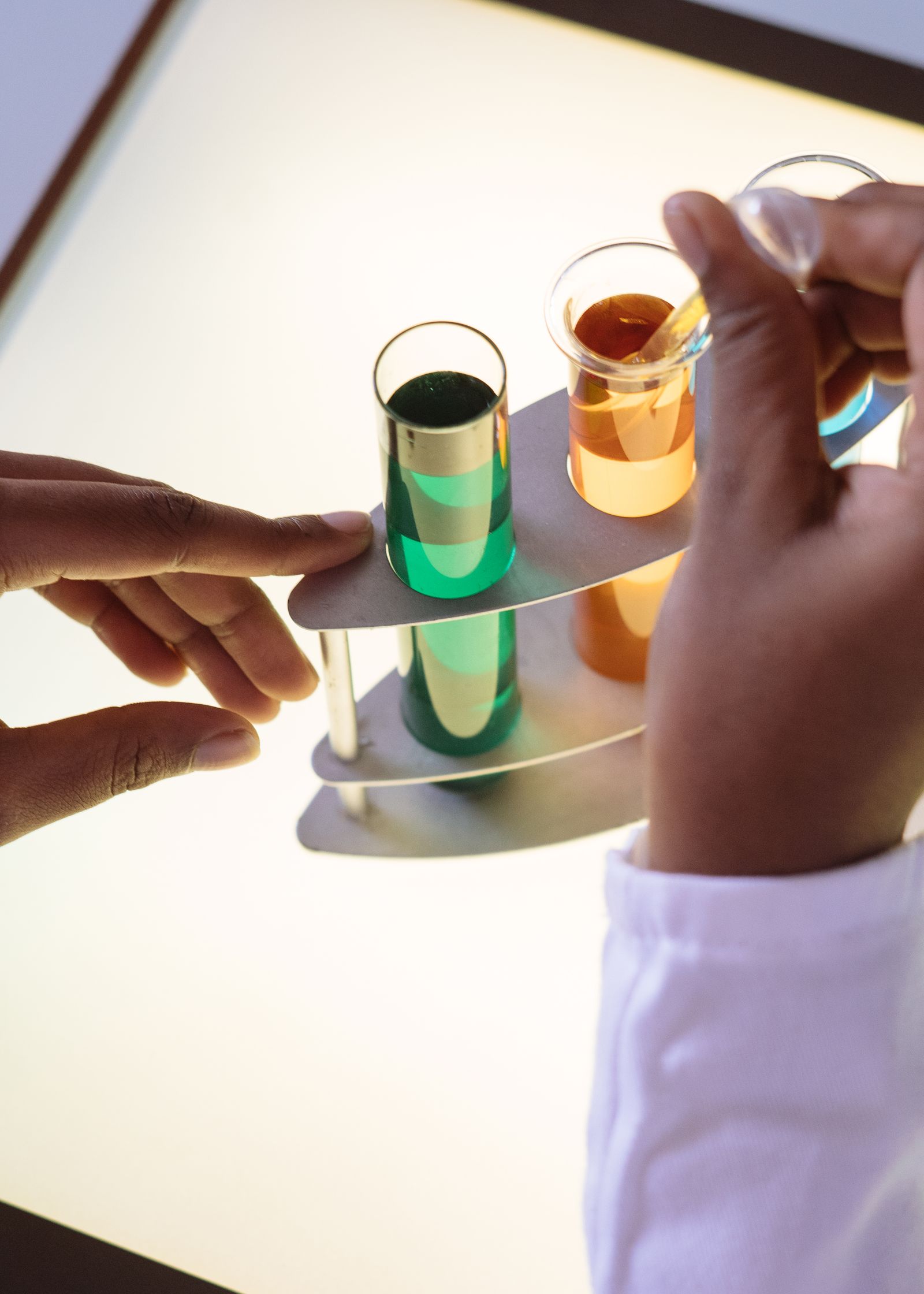 Hands working with coloured samples in glass tubes